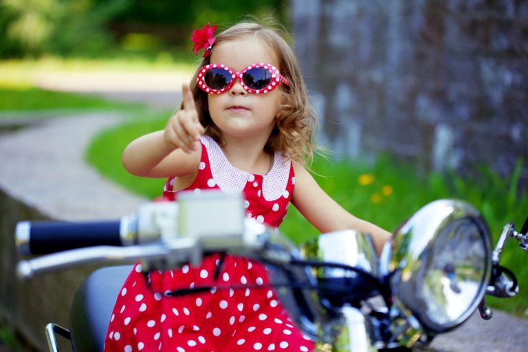 naming ceremonies Child aged about 4 with red polkadot party dress and matching sunglasses, sitting on a motorbike.