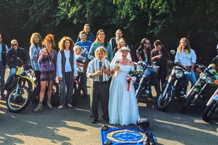 Weddings Male and female couple wearing wedding outfits with bikers and their motorbikes forming a circle around them.